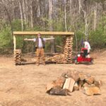 Man standing with outstretched arms in front of stack of firewood